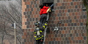 Feuerwehrleute retten Menschen, die aus dem Fesnter des Wohnhauses absteigen