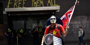 Ein Mann mit Guy-Fawkes-Maske steht vor dem Eingang eines Hotels