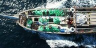 Ein Boot, auf dem grüne Plastiksäcke tranportiert werden, aus der Vogelperspektive aufgenommen