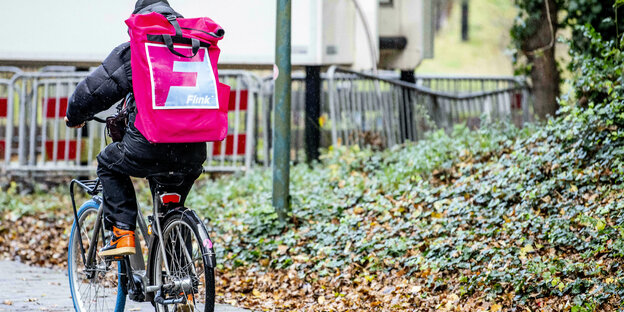 Ein Fahrradbote mit pinkfarbenem Rucksack von hinten fotografiert
