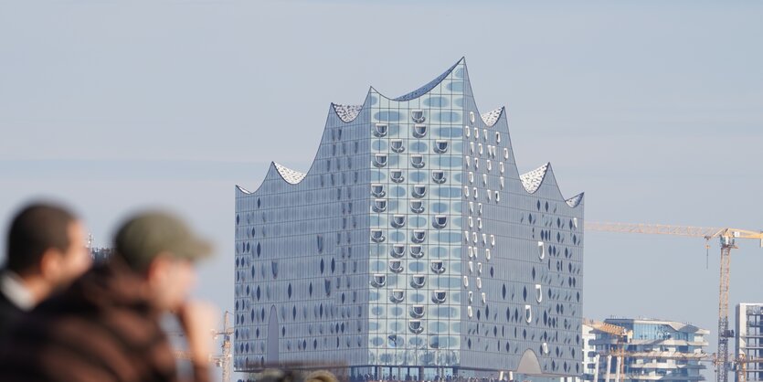 Passanten sitzen auf einer Kaimauer am Hamburger Fischmarkt. Im Hintergrund ist die Elbphilharmonie zu sehen