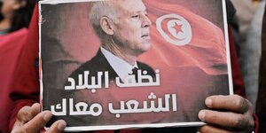 Jemand hält ein Plakat in den Händen mit dem Portrait des tunesischen Präsidenten Kais Saied