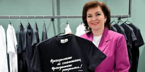 Eine Frau im pinkfarbigen Jacket hält ein T-Shirt mit einer kyrillischen Aufschrift hoch