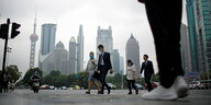 Menschen an einem grauen Tag gehen Menschen mit Masken vor den Hochhäusern Shanghais