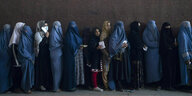 Frauen mit und ohne Burka stehen in einer Warteschlange