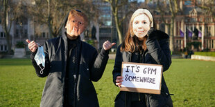 Mit Masken von Johnson und seiner Frau Carrie protestieren 2 Menschen "Irgendwo ist es 18 Uhr", bezieht sich auf einen Partyaufruf in der Downing Street