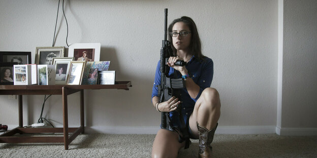 Eine posiert mit einem schwerem Gewehr in ihrem Wohnzimmer