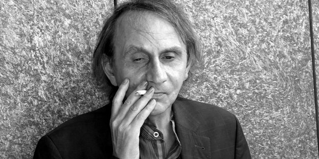 Der Schriftsteller Michel Houellebecq mit Zigarette vor Tapete