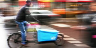 Ein verschwommenes Bild zeigt einen Lastenradfahrer auf einer PKW Straße.