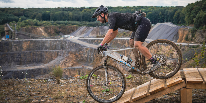 Mlountainbiker fährt vor einem Steinbruch und einem Wald , er ist verschlammt