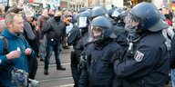 Links steht eine Person ohne Maske, rechts Polizist:nnen. Im Hintergrund sind weitere Polizist:innen sowie Demonstrierende