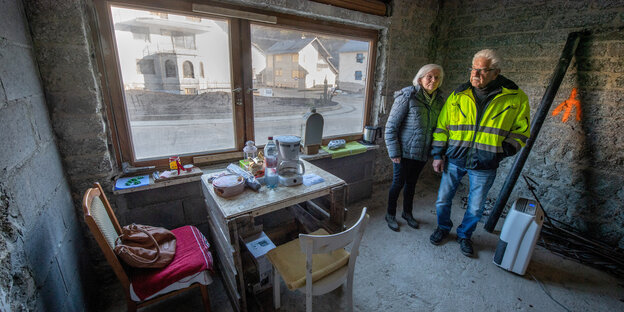 Eine Frau und ein Mann, beide weißhaarig, in einem entkernten Zimmer neben einem Tisch aus Europaletten
