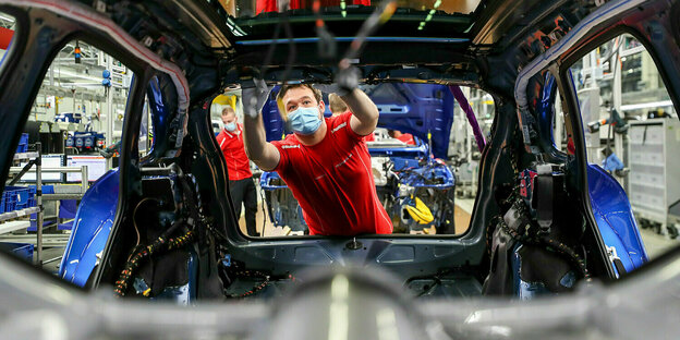Ein mechaniker mit Mundschutz bei der Arbeit an einer Autokarosserie
