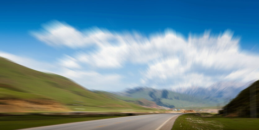 Straße vor grünen Hügeln und blauem Himmel