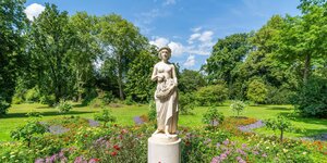 Eine Statue, eine Frau zeigt, steht inmitten von vielen blühenden Sommerblumen im Park von Schloss Park Sanssouci in Potsam