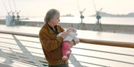 Ein älterer Mann mit brauner Wildlederjacke und Baby im Arm am Hafen von Marseille