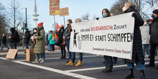 Menschen stehen mit einem Transparent "Impfen statt schimpfen" auf einer Straße in Hamburg