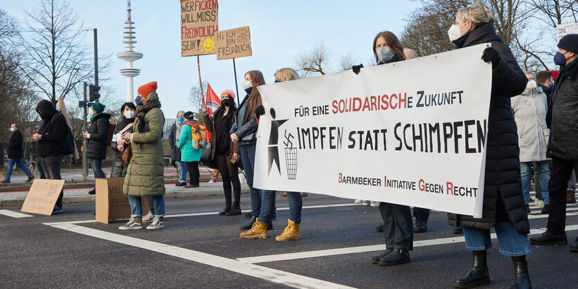 Menschen stehen mit einem Transparent "Impfen statt schimpfen" auf einer Straße in Hamburg