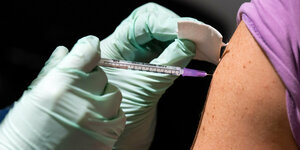 Eine Spritze sticht während einer Impfung in einen Oberarm