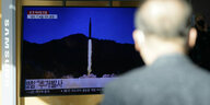 ein Mann vor einem Bildschirm, auf dem ein Raketenstart zu sehen ist