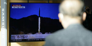 ein Mann vor einem Bildschirm, auf dem ein Raketenstart zu sehen ist