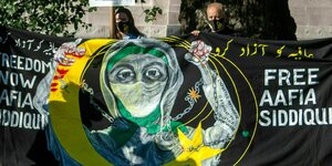 Protest mit einem Bannert: Frau in Ketten und Kopftuch und der Botschaft:Free Aafia Siddiqui