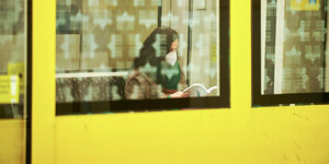 Frau mit Maske im Fenster eines gelben Berliner U-Bahn-Waggon