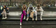 Jugendliche mit Smartphones sitzen auf einem Brunnenrand