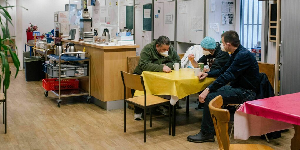 3 Männer sitzen um einen Tisch mit gelber Plastiktischdecke