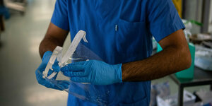 Pfleger in blauer Kleidung reinigt ene Gesichtsmaske