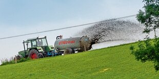 Ein Traktor zieht eine Landwirtschaftsmaschine, mit der Gülle auf ein gemähtes Feld verteilt wird.