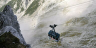 Die Karwendelbahn hängt an Seilen zwischen Bergen, dahinter sind Wolken