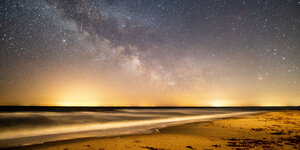 Ein Strand am Sonnenuntergang und viele Sterne am Himmel.