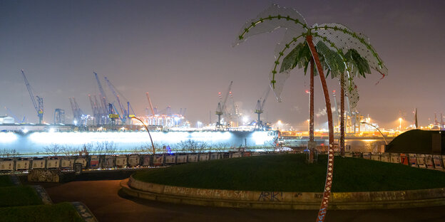 Künstliche Palmen auf einer Grasinsel, dahinter der Hamburger Hafen