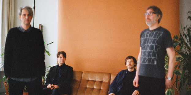 Die vier Bandmitglieder in einem Zimmer vor orangener Tapete