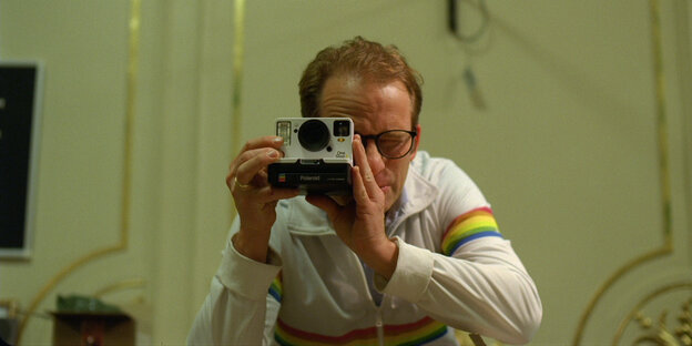 Ein Mann blickt durch eine Polaroidkamera ins Bild.
