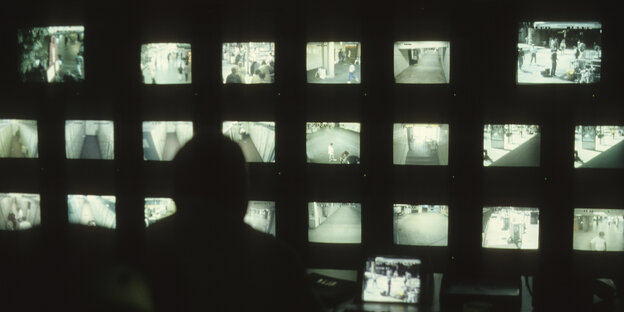 Eine Person schaut auf eine Wand von Überwachungsmonitoren