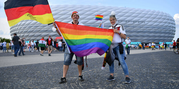 Zwei Sportfans mit Deutschland- und LGBTIQ-Fahne vor der Arena in München