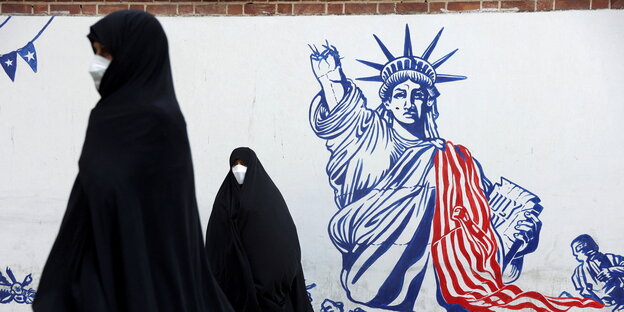 Graffiti der Freiheitsstatue mit amputiertem Arm, davor stehen zwei Frauen im Tschador
