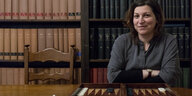 Eine Frau vor einem Bücherregal, vor ihr auf dem Tisch ein Backgammon-Spiel