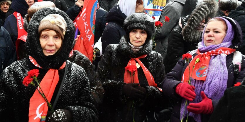 Menschen mit Pelzmnteln und Mützen halten Nelken und Flaggen in der Hand