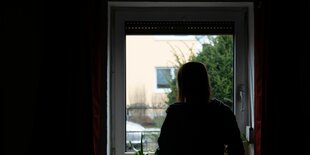 Eine Person steht in einem dunklen Raum in einem Fenster und schaut nach draußen