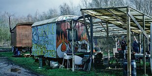 Bauwagen und ein Holzverschlag stehen auf einer Wiese.