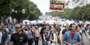 Eine Frau in weiß auf einer Demonstration trägt ein Schild mit der Aufschrift: "Nein zur Impfapartheit. Nie wieder Faschismus"