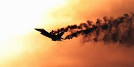 Militärjet des Typs F-16 Falcon fliegt vor orangefarbenem Himmel und zieht schwarzen Ruß nach sich.