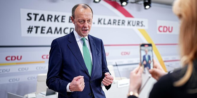 Friedrich Merz ballt die Fäuste und wird dabei von einer Person mit dem Handy für die Social-Media-Kanäle aufgenommen