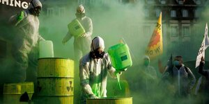 Mehrere Menschen in weißen Schutzanzügen und schwarzen Gasmasken übergießen am 19.01.2022 in Straßburg gelbe Atommüll- und rote Gas-Fässer mit giftgrüner Farbe, um gegen Greenwashing zu demonstrieren. Atomkraft und fossiles Gas sollen von der EU ein Öko-L