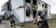 Zwei Feuerwehrmänner stehen in Atemschutzmasken vor einer ausgebrannten Containerwohnung