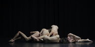 Fünf TänzerInnen liegen nackt auf einer schwarzen Bühne