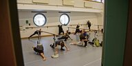 Tänzerinnen und Tänzer machen Dehnübungen in einer Halle.